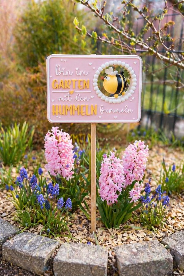 IMG_1631 Rosafarbenes Gartenschild mit Hummelmotiv und Spruch zwischen blühenden Frühlingsblumen